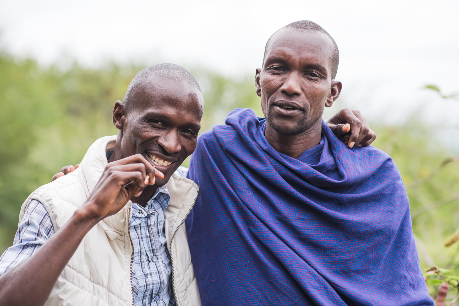 Two men standing together outdoors, one with his arm around the other